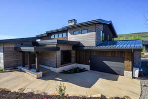 Modern home featuring a standing seam roof, stone siding, a garage, driveway, and a chimney