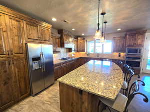 Kitchen with a kitchen breakfast bar, a kitchen island, light stone countertops, stainless steel appliances, and tasteful backsplash