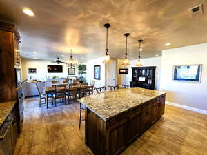 Kitchen with a kitchen breakfast bar, light stone countertops, dark wood finish cabinetry, a center island, and open floor plan