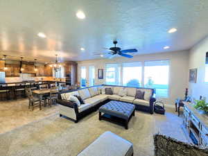 Living area with suspended lighting, light colored carpet, plenty of natural light, a textured ceiling, and ceiling fan