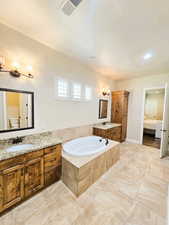 Ensuite bathroom with two vanities, a garden tub, and suspended lighting