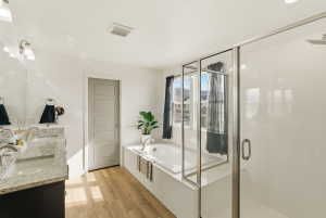 Full bathroom with a shower stall, a garden tub, light wood finished floors, and double vanity