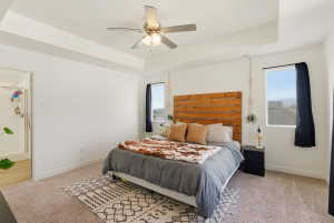 Bedroom featuring a tray ceiling, light carpet, ceiling fan, multiple windows, and ensuite bathroom