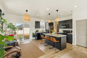 Kitchen featuring dark cabinetry, hanging light fixtures, a kitchen island, black appliances, and a breakfast bar