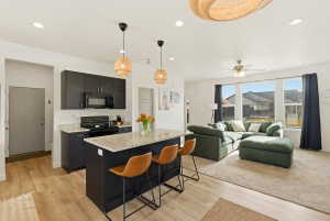Kitchen with dark cabinets, hanging light fixtures, a kitchen bar, black appliances, and light stone counters