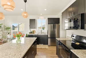 Kitchen with black appliances, hanging light fixtures, light stone countertops, light wood finished floors, and dark cabinetry