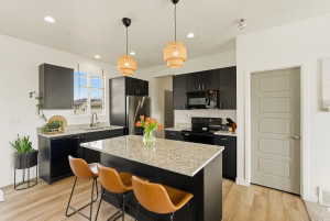 Kitchen with dark cabinetry, hanging light fixtures, black appliances, light wood-style flooring, and a center island