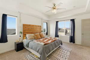 Bedroom featuring a raised ceiling, light carpet, and a ceiling fan