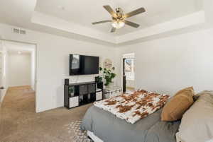 Carpeted bedroom featuring a tray ceiling, a ceiling fan, and ensuite bath