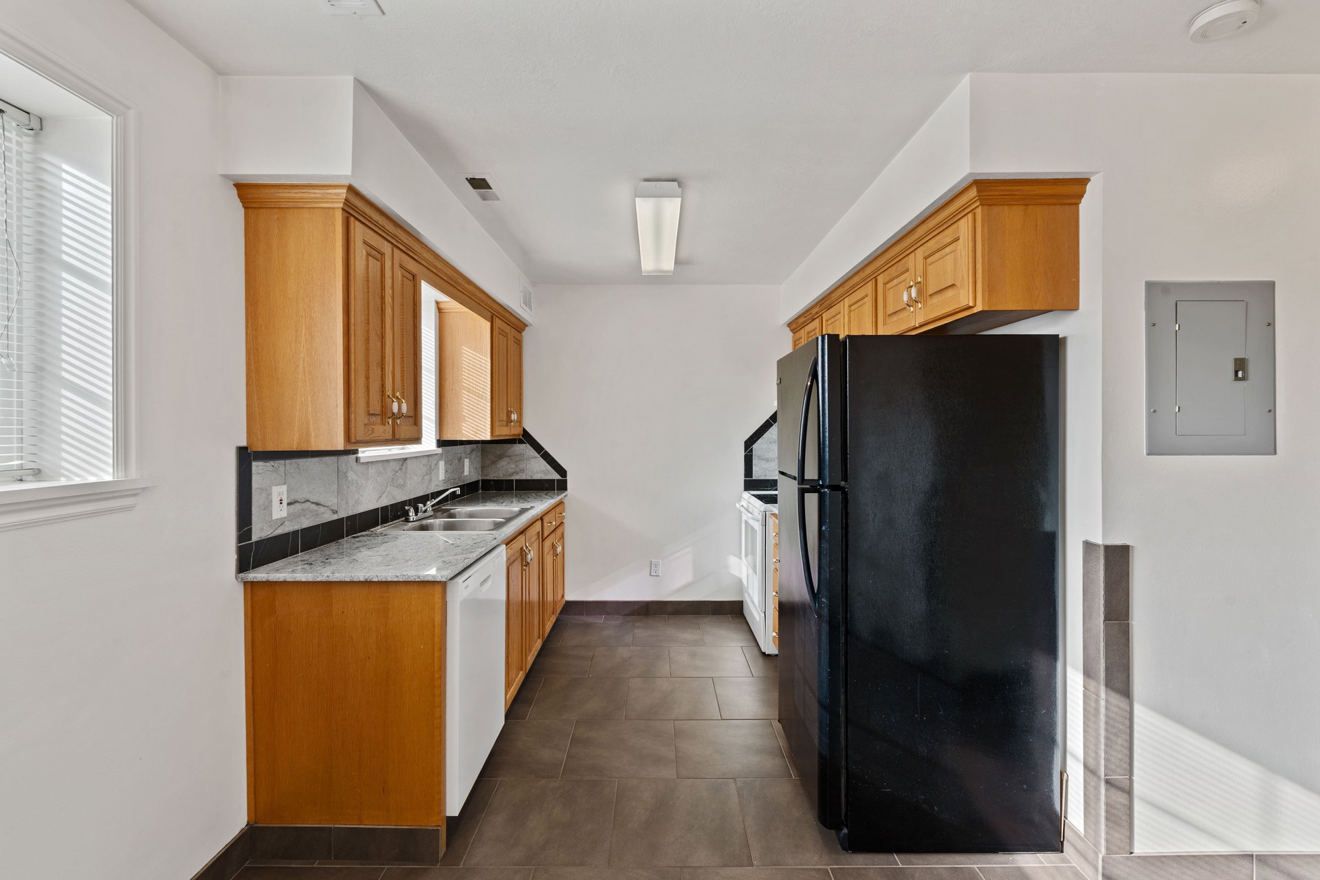 Kitchen with white appliances, backsplash, electric panel, light stone counters, and wood finish cabinetry