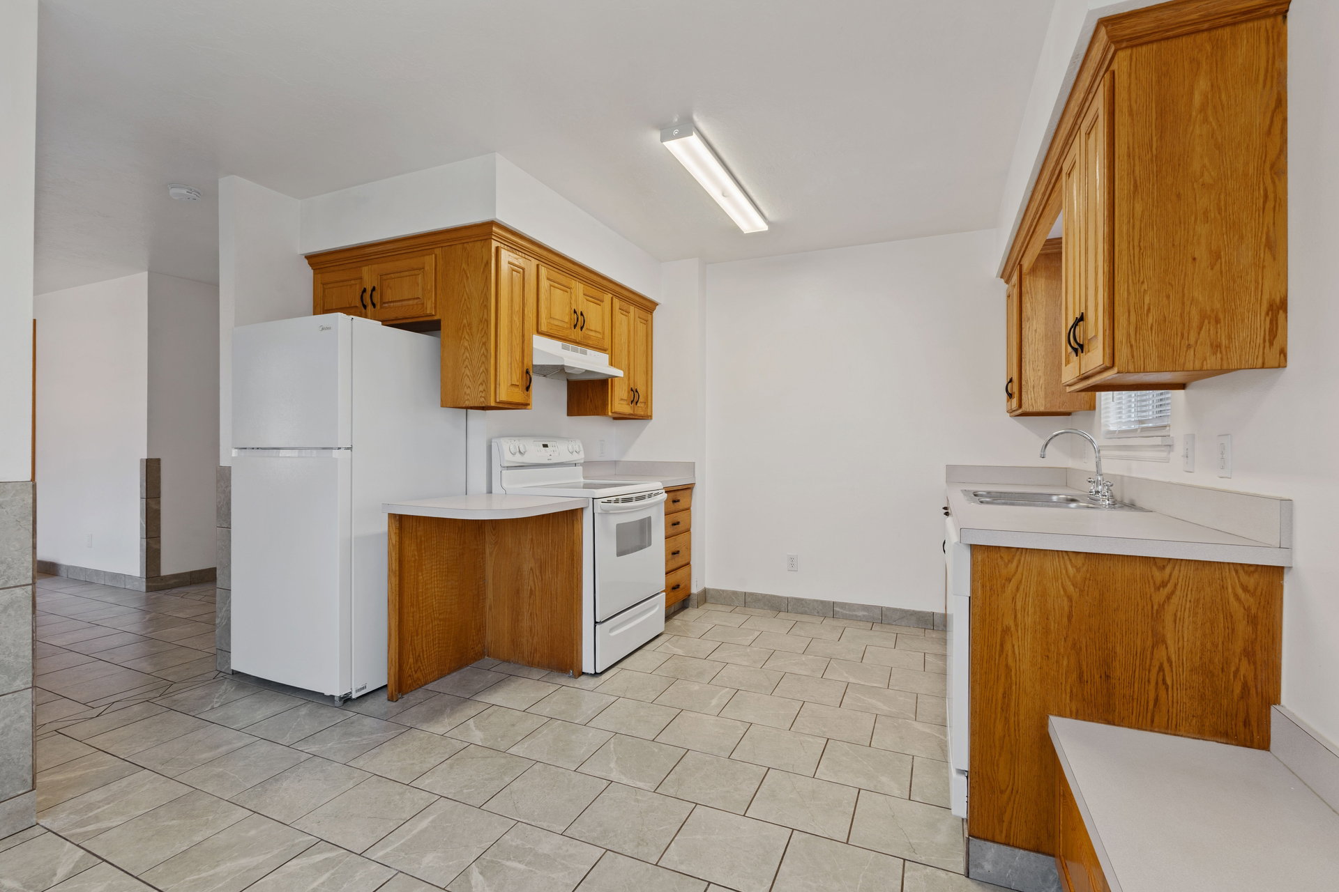 Kitchen with white appliances, light countertops, wood finish cabinetry, and light tile patterned flooring