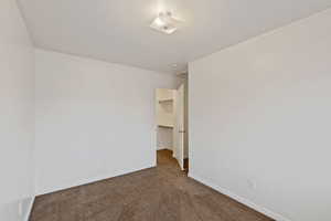 Unfurnished bedroom with a walk in closet and dark carpet