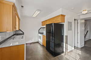 Kitchen with freestanding refrigerator, decorative backsplash, electric stove, light stone countertops, and electric panel