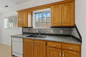 Kitchen featuring wood finish cabinets, white dishwasher, backsplash, and plenty of natural light