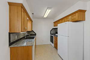 Kitchen featuring white appliances, decorative backsplash, light stone countertops, light floors, and wood finish cabinets