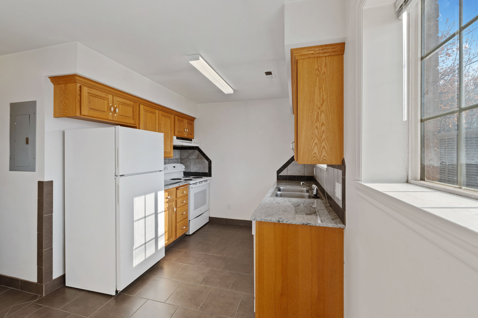 Kitchen with light stone counters, white appliances, electric panel, tasteful backsplash, and wood finish cabinetry
