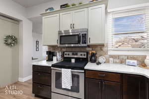 Kitchen with stainless steel appliances, light stone counters, light wood-style flooring, decorative backsplash, and dual tone cabinets