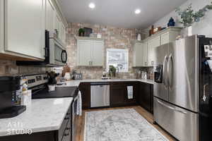 Kitchen with stainless steel appliances, decorative backsplash, light wood-style floors, and light stone counters