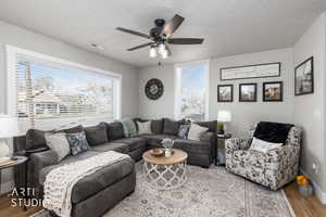 Living room featuring wood finished floors, plenty of natural light, a ceiling fan, and a textured ceiling