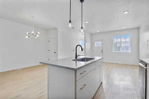 Kitchen featuring light wood finished floors, a textured ceiling, white cabinetry, stainless steel dishwasher, and a center island with sink