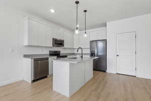 Kitchen featuring stainless steel appliances, pendant lighting, light wood finished floors, a kitchen island with sink, and modern cabinets