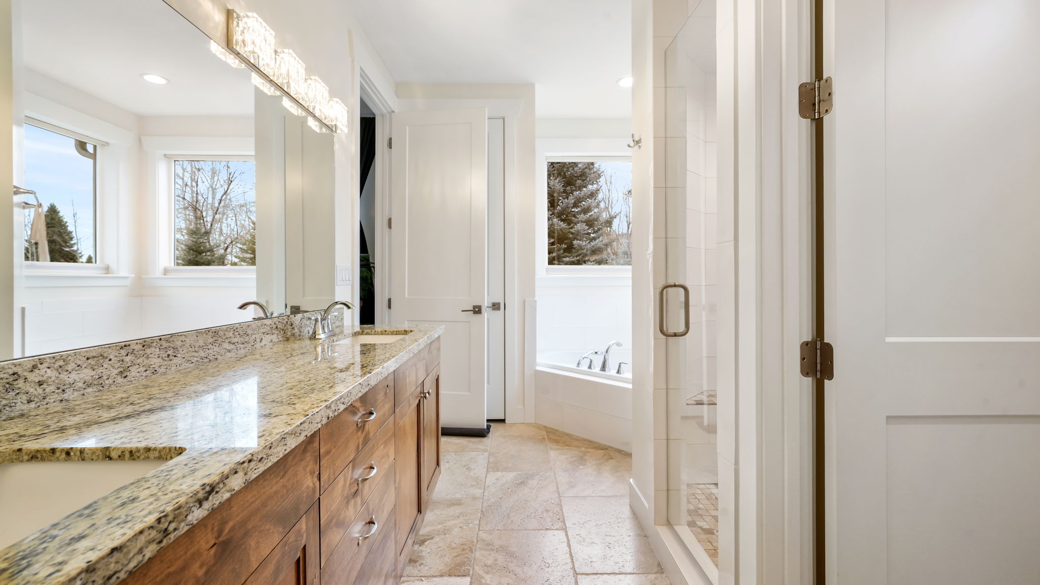 Bathroom featuring a dual-sink wood-finish vanity with a stone countertop, a large mirror, a decorative light fixture, and a glass-enclosed shower