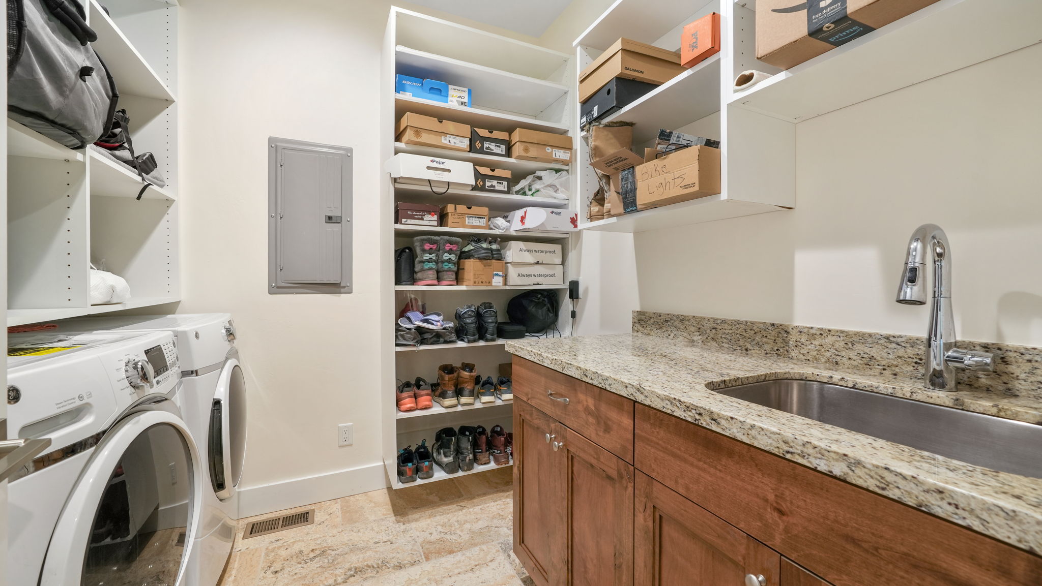 Dedicated laundry area featuring a front-loading washer and dryer, extensive built-in shelving, a stainless steel sink, a granite-finish countertop, and wood-finish cabinetry