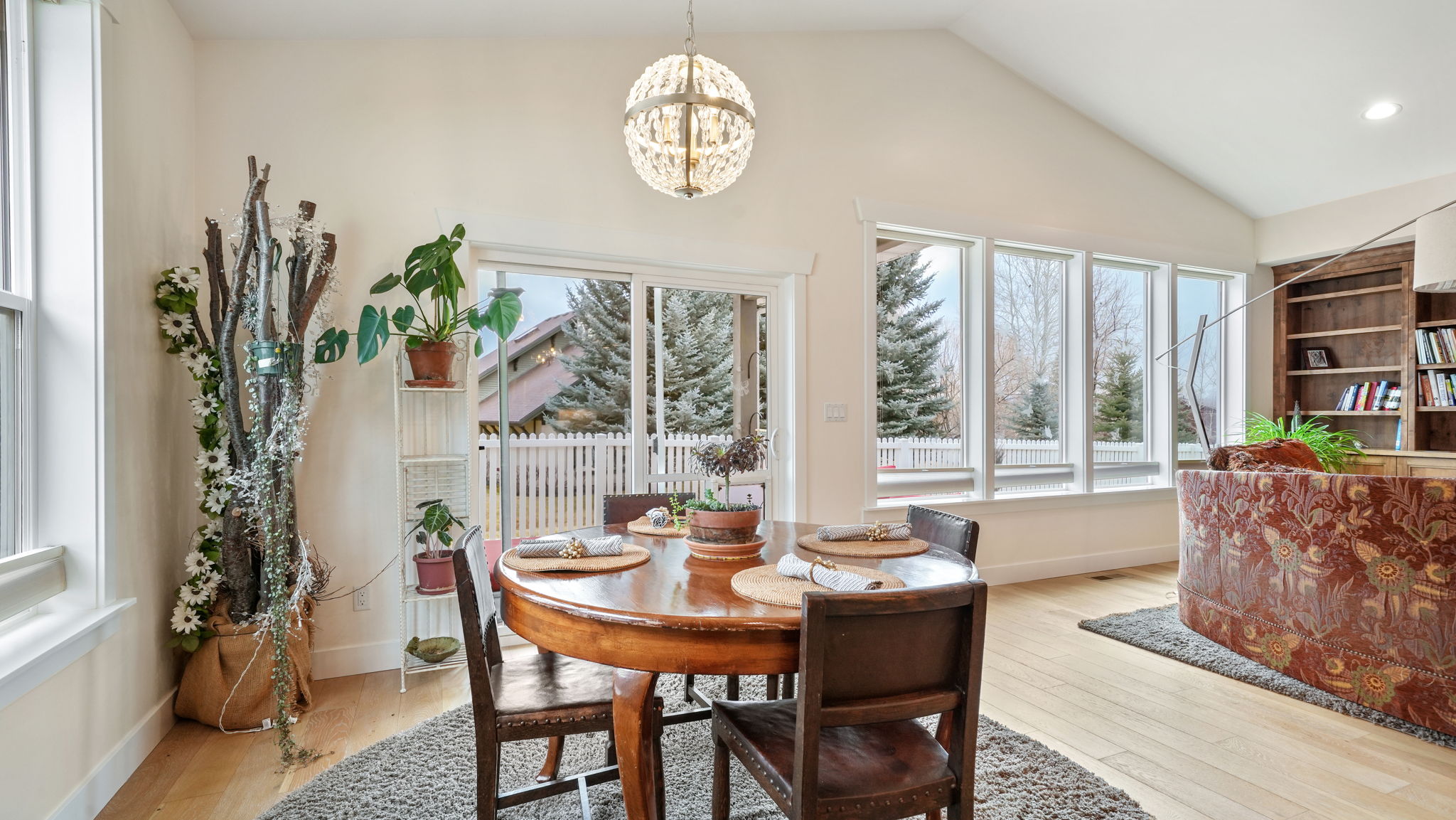 Vaulted ceiling dining area featuring wood-finish flooring, a contemporary chandelier, and a wall of windows