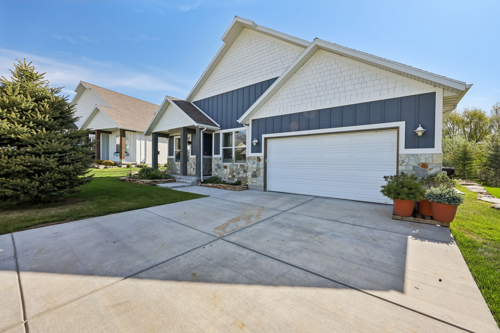 Contemporary exterior featuring a two-car garage, stone accents, shingle siding, a covered entry, and a concrete driveway