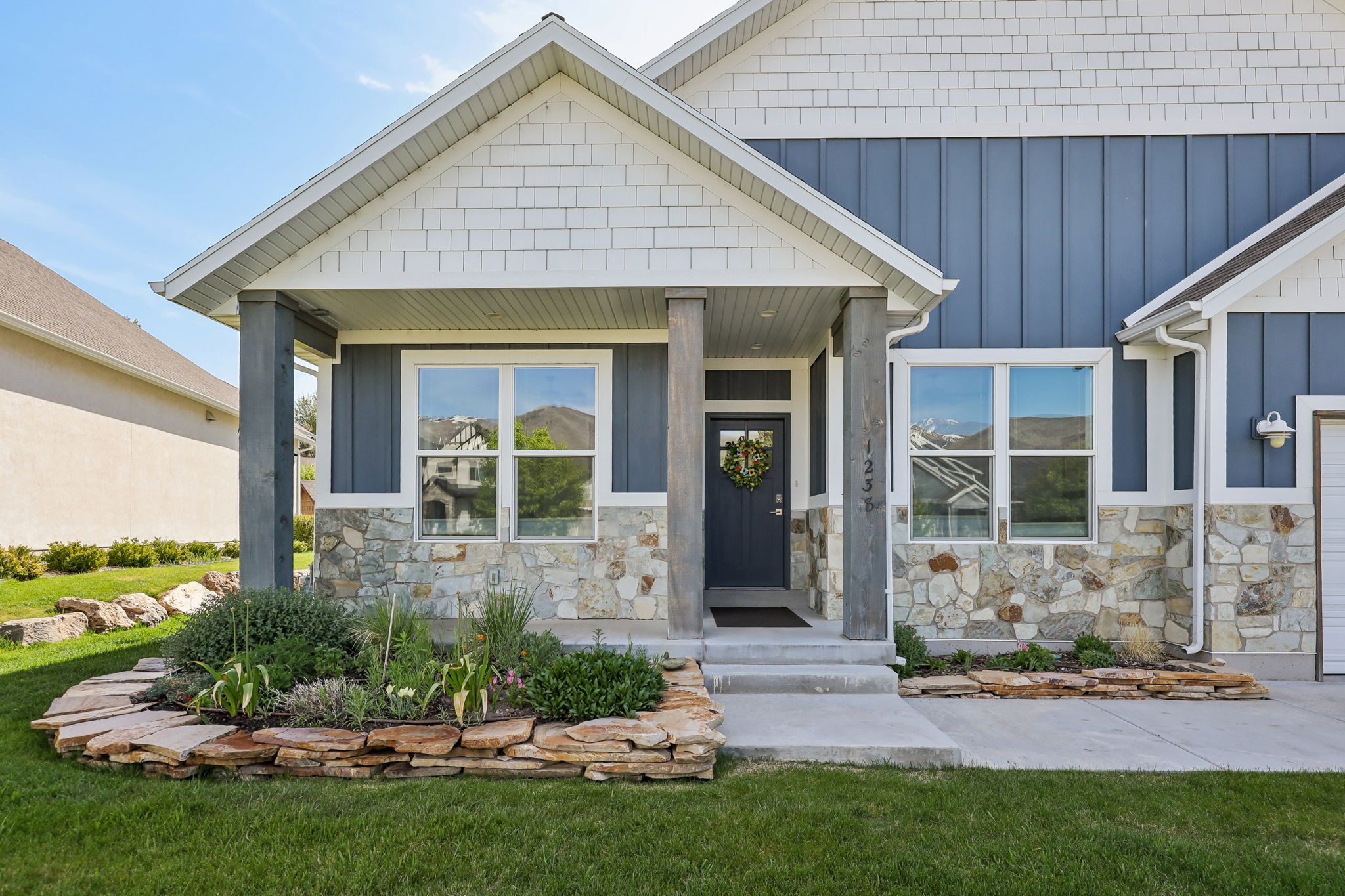 Front exterior featuring a covered porch with stone pillars, board and batten siding, horizontal shingle accents, and a stone facade