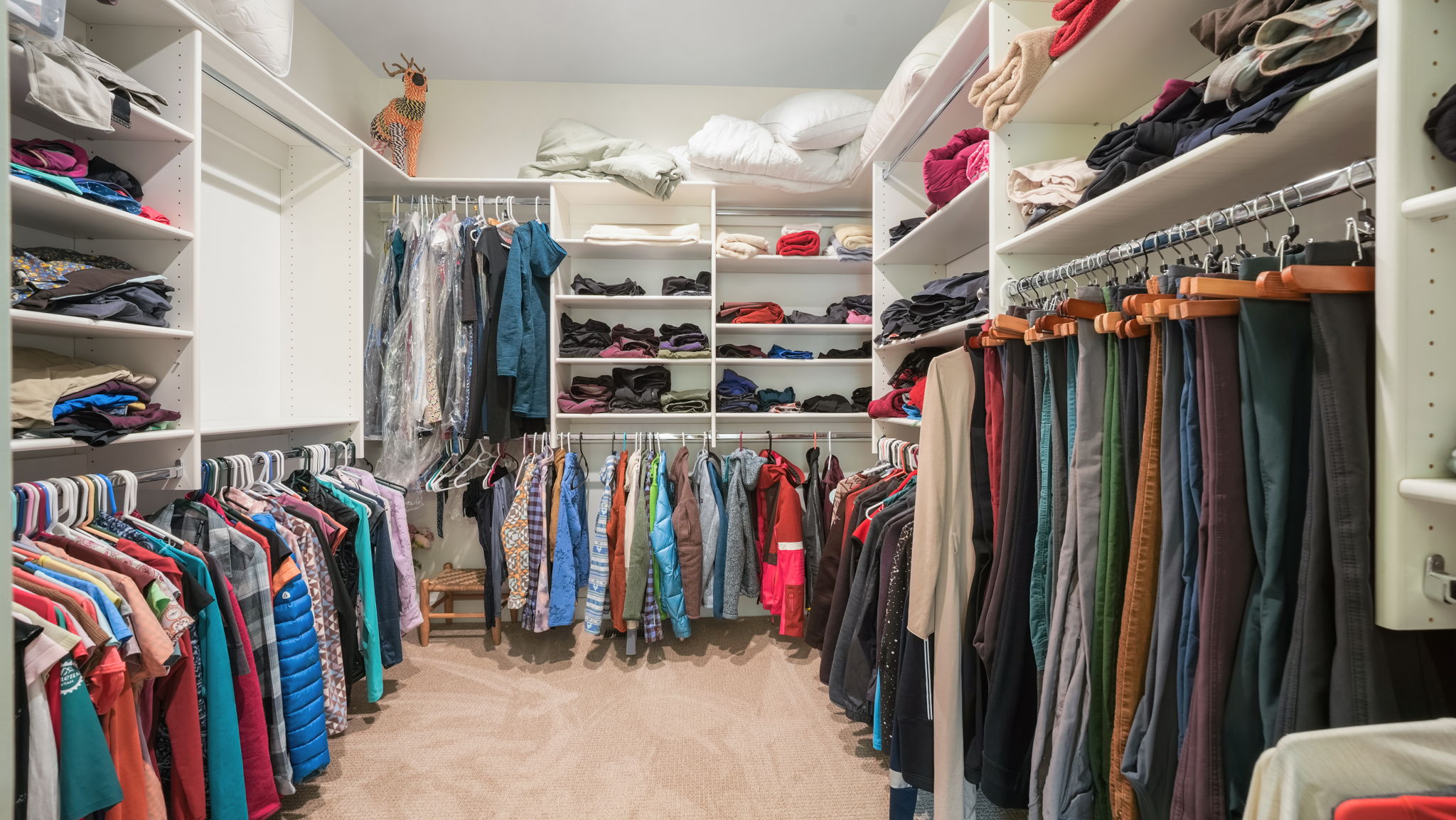Walk-in closet featuring built-in shelving, multiple hanging rods, corner shelving units, and carpet flooring