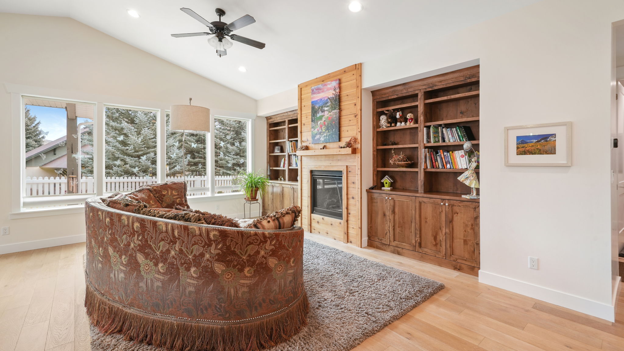 Bright living space featuring vaulted ceilings, light wood-finish flooring, and multiple large windows