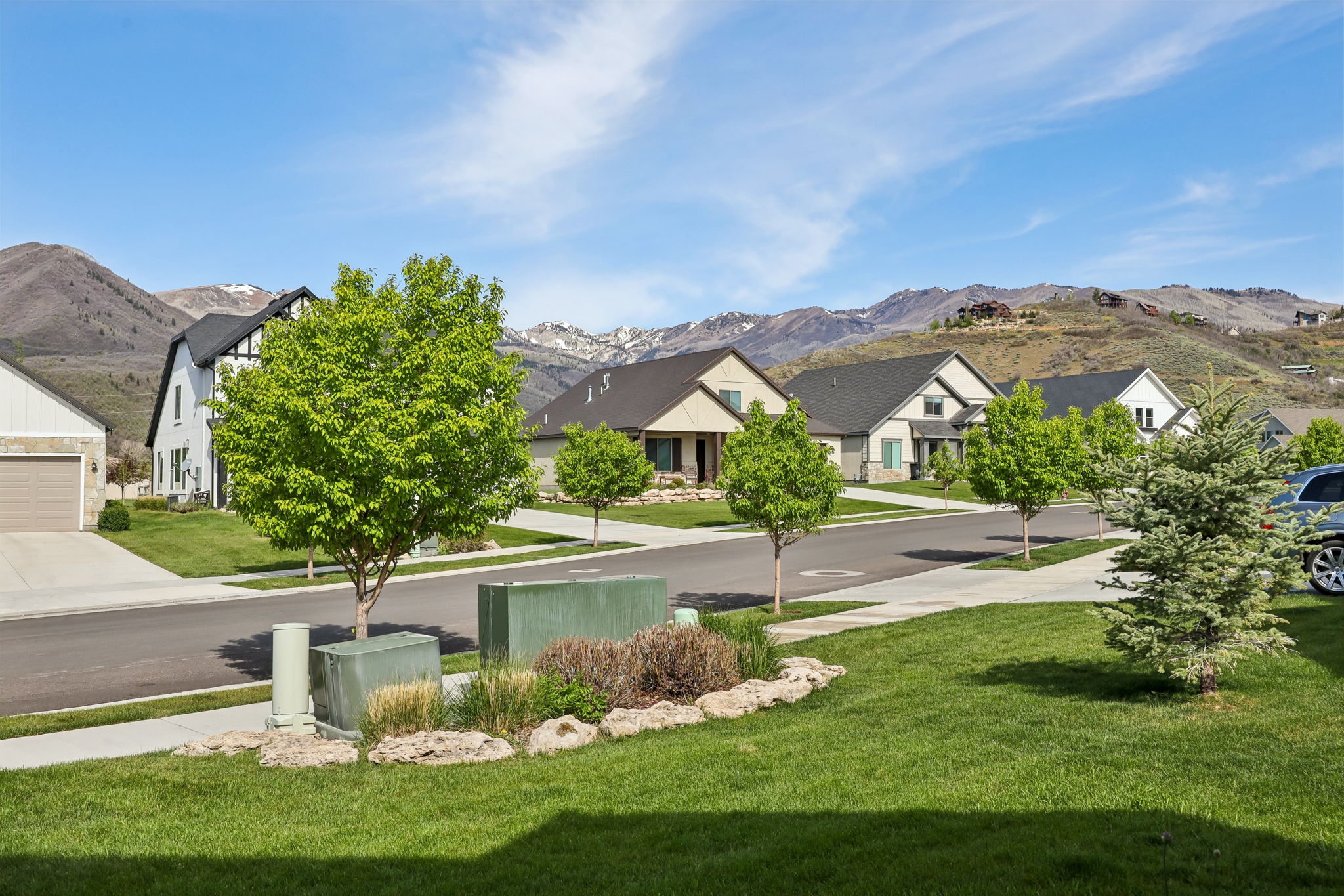 Residential street with paved sidewalks and mature trees, featuring varied architectural styles including a modern farmhouse and stucco exteriors