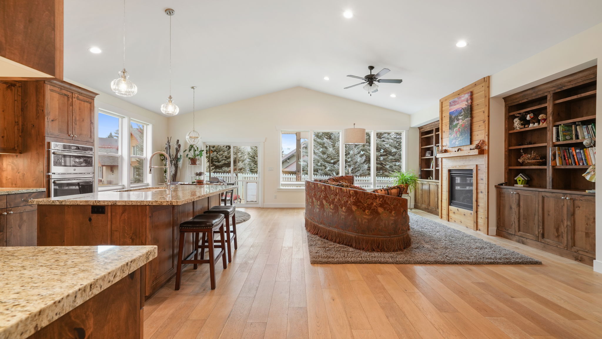 Vaulted ceiling living area featuring light wood-finish flooring, a stone fireplace with wood surround, built-in shelving, and recessed lighting
