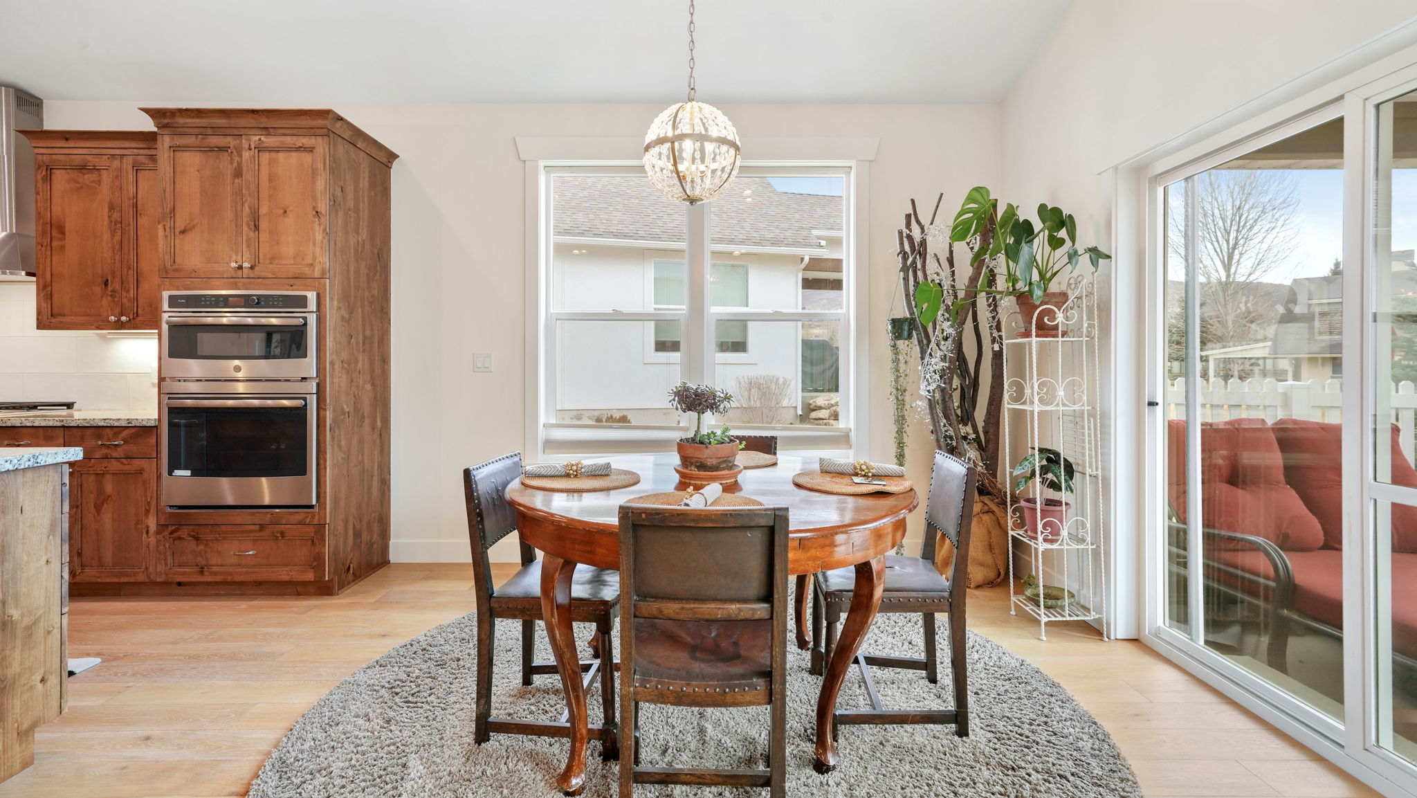 Open-concept dining area featuring light wood-finish flooring, a contemporary chandelier, a large window, and a sliding glass door