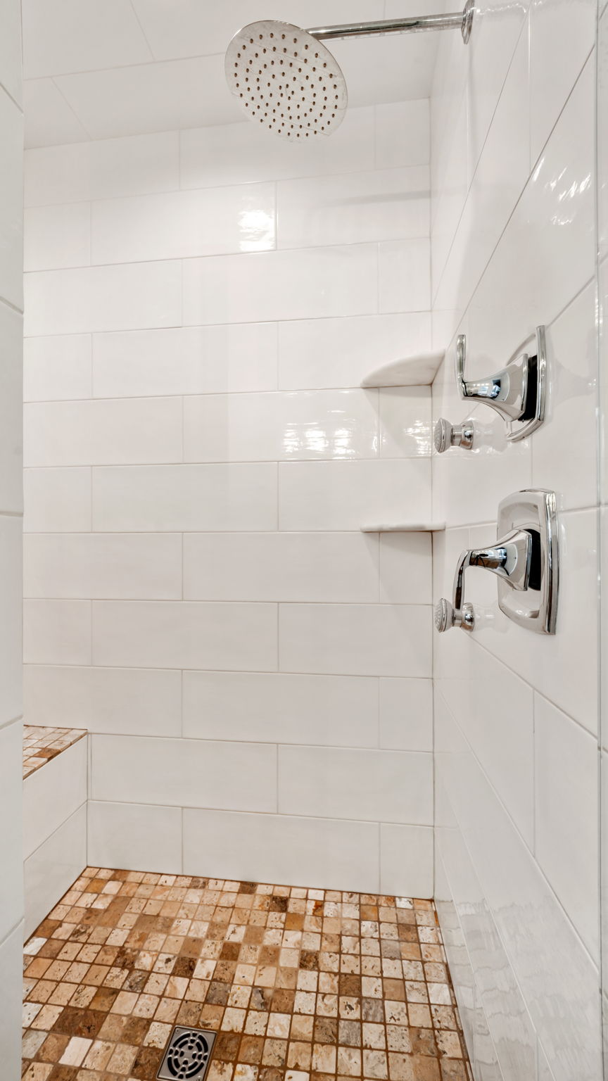 Shower with white subway tile walls, a built-in bench, a rain showerhead, chrome fixtures, and natural stone mosaic floor tiling