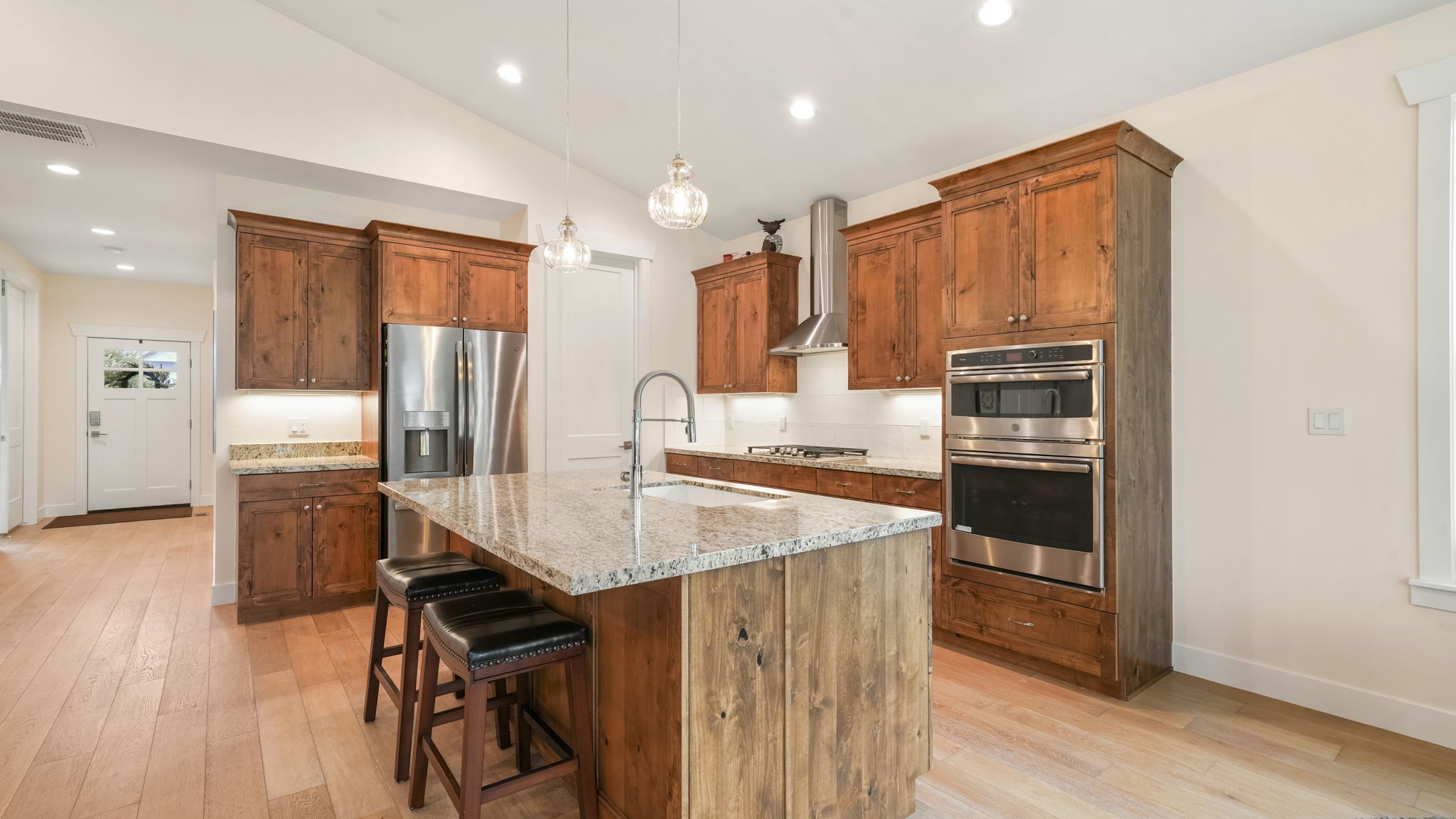 Gourmet kitchen featuring a substantial central island with seating, granite countertops, wood-finish cabinetry, stainless steel appliances, and light wood-finish flooring