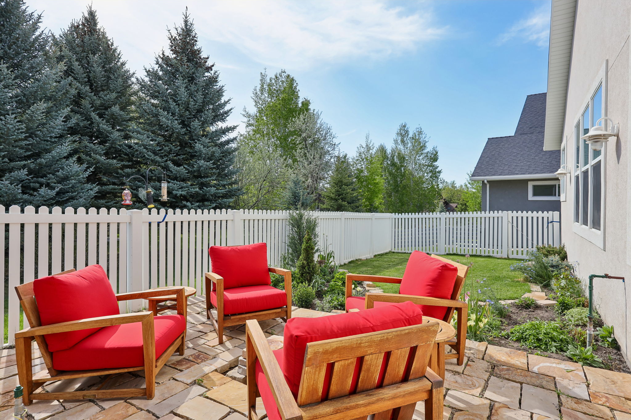 Stone-paved patio with a white picket fence, surrounded by mature evergreen trees