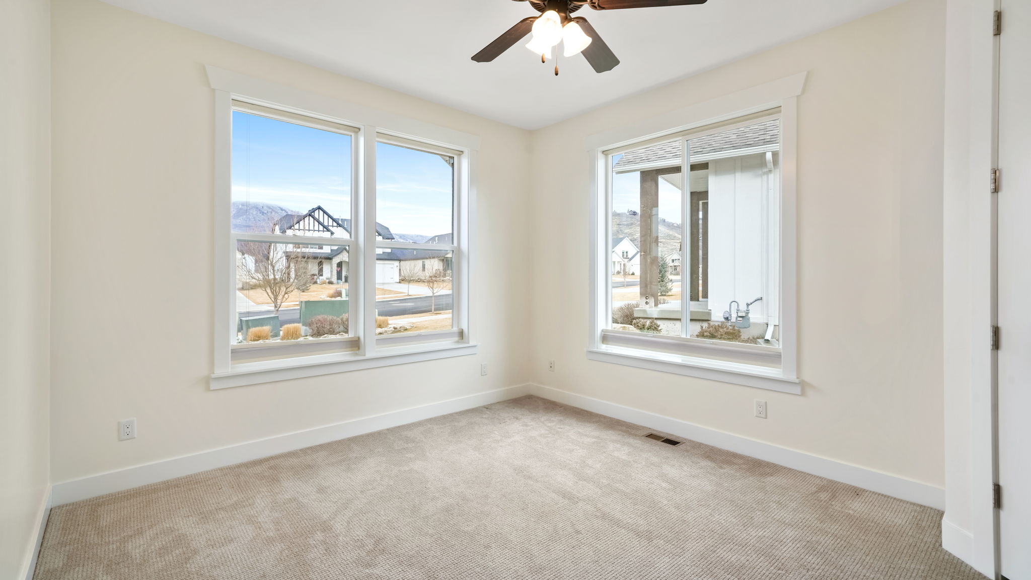 Bright room featuring two windows, neutral carpeting, and a ceiling fan with integrated lighting