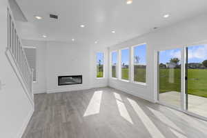 Unfurnished living room with recessed lighting, light wood-style flooring, and a glass covered fireplace