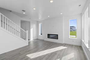 Unfurnished living room with a glass covered fireplace, recessed lighting, light wood-style flooring, and healthy amount of natural light