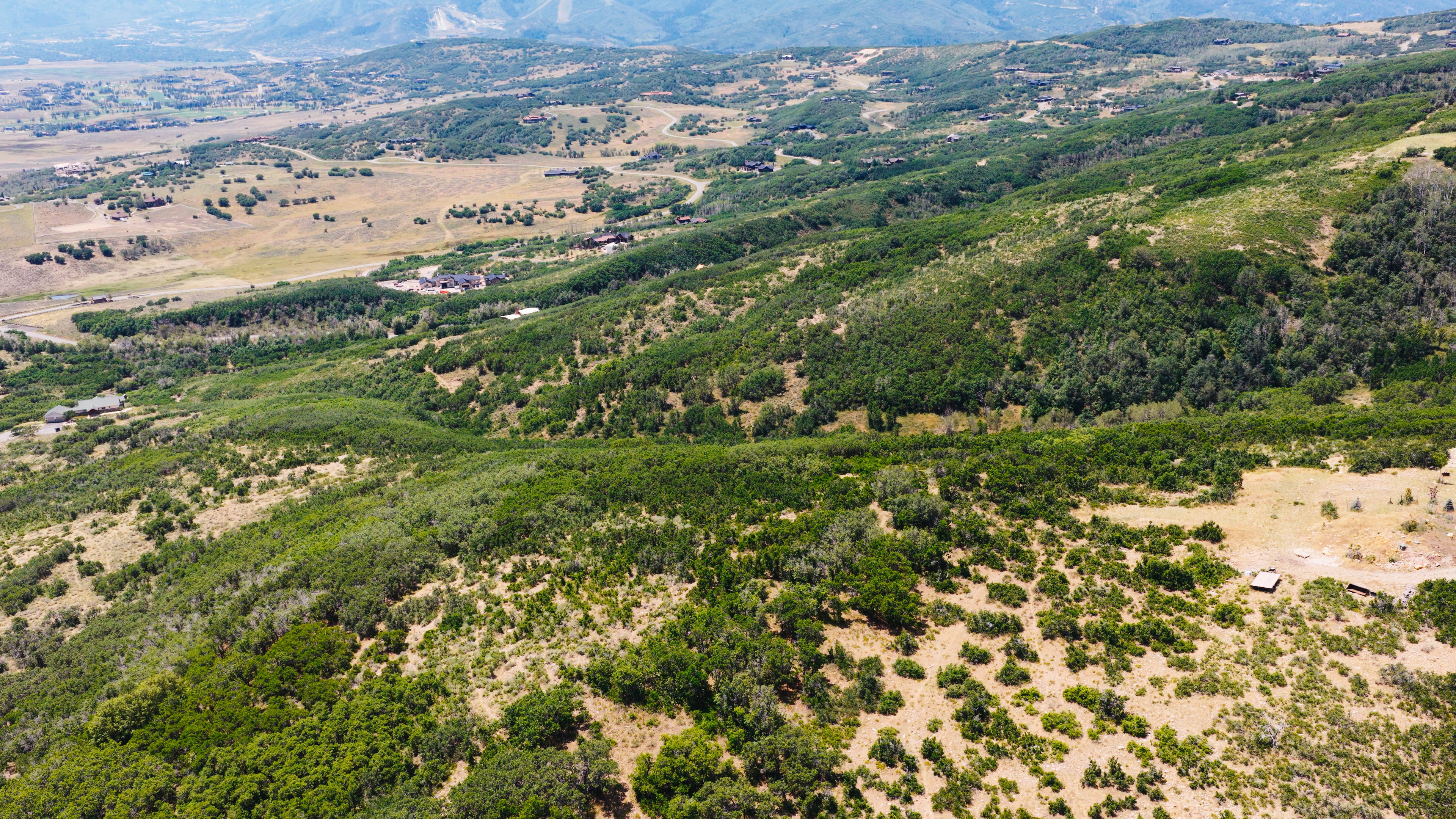 Expansive aerial landscape featuring rolling hills, varied terrain, and distant mountain ranges