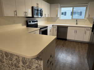 Kitchen featuring a peninsula, stainless steel appliances, white cabinetry, and light countertops