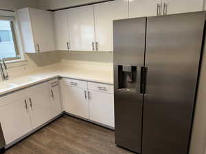 Kitchen with stainless steel fridge, white cabinetry, dark wood-type flooring, and light countertops