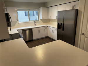 Kitchen featuring stainless steel appliances, light countertops, white cabinetry, and dark wood-type flooring