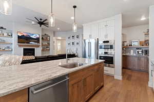 Kitchen featuring pendant lighting, open floor plan, stainless steel appliances, dual tone cabinetry, and a lit fireplace