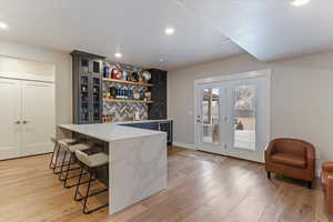 Bar featuring open shelves, light stone counters, glass insert cabinets, light wood-style flooring, and recessed lighting