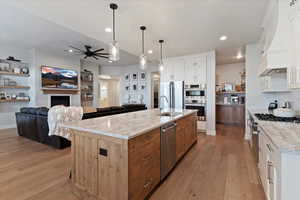Kitchen featuring a warm lit fireplace, two tone color scheme, light wood-style flooring, open floor plan, and pendant lighting