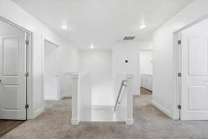 Hallway with an upstairs landing, light colored carpet, recessed lighting, and washer and dryer
