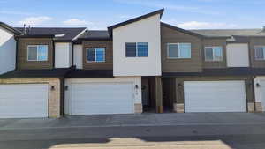 View of front of home with stone siding, a garage, driveway, and a shingled roof